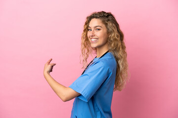 Young surgeon doctor woman isolated on pink background pointing back