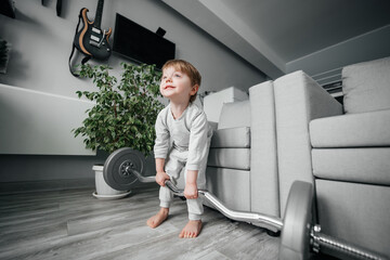 little boy lifts a barbell in a room on a gray background