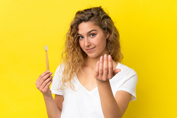 Young caucasian woman holding a brushing teeth isolated on yellow background inviting to come with hand. Happy that you came