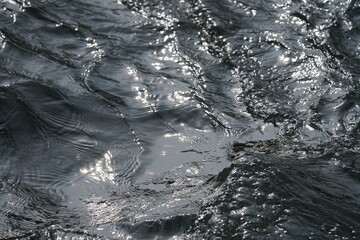 Fließendes Wasser in einem Fluss und mit Sonnenlicht, welches sich im Wasser spiegelt und reflektiert