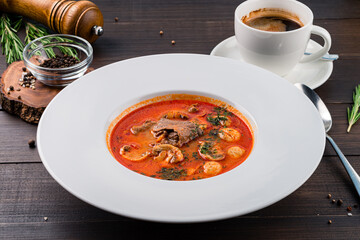 Hot soup with meat and mushrooms in a white plate on wooden background