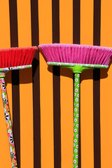 Two broomsticks with red and pink bristles and colorful patterns in front of a wall with vertical...