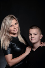 Young attractive blonde mother leans her hand on her teenager son. Studio photo on a dark background