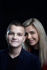 A young attractive mother is standing behind her white teenage son and both are smiling. Studio photo on a dark background