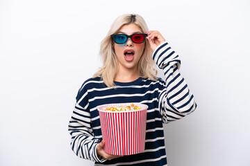 Obraz premium Young Russian woman isolated on white background surprised with 3d glasses and holding a big bucket of popcorns