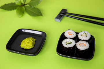 Sushi hosomaki maki set with wasabi paste in vibrant green color background.