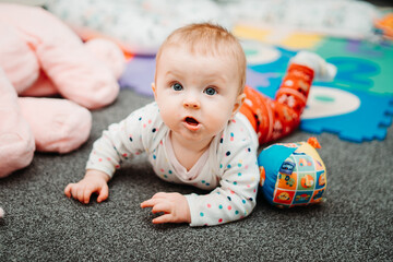 Small 5-month old baby girl lying on the floor, playing with toys