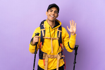 African American man with backpack and trekking poles over isolated background saluting with hand with happy expression
