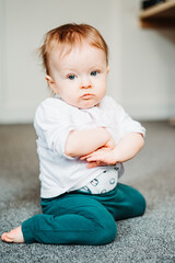 8-month-old baby girl sitting grumpy with  her hands crossed on her chest