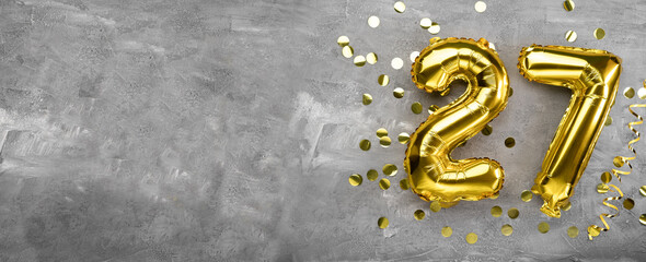 Yellow foil balloon number, number twenty-seven on a concrete background. Birthday card with...