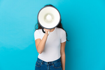 Fototapeta na wymiar Teenager Russian girl isolated on blue background shouting through a megaphone to announce something