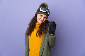 Teenager Russian girl with snowboarding glasses isolated on purple background saluting with hand with happy expression