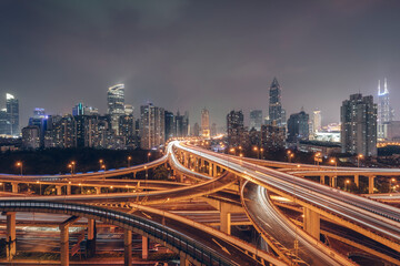 Fototapeta premium Urban overpasses with lights on at night and the urban background in the distance