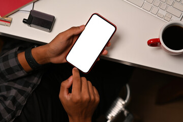 Top view close up of a young man sitting in the office typing on a touchscreen on a smartphone with a blank white screen, for business and technology concept.