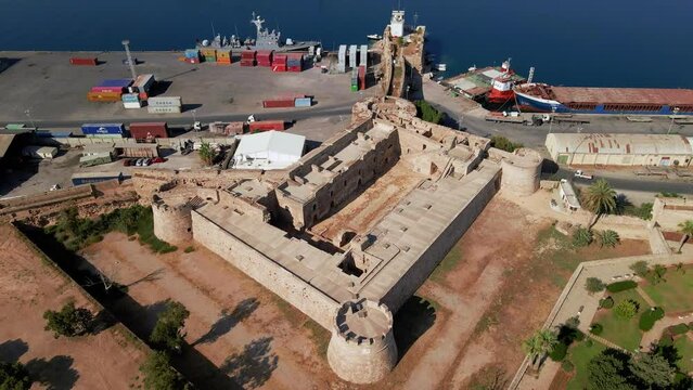 Aerial 4k Othello Castle medieval building in Famagusta Walled City in North Cyprus which is surrounded with old town streets, sea port and touristic attractions with blue sky in sunny day, Cyprus