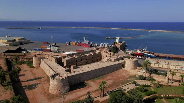 Aerial 4k Othello Castle medieval building in Famagusta Walled City in North Cyprus which is surrounded with old town streets, sea port and touristic attractions with blue sky in sunny day, Cyprus