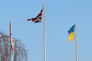 England Great Britain and Ukraine flags on poles high up blowing in the blue skies 