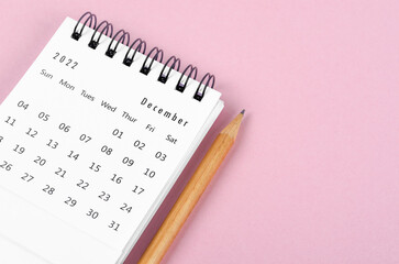 December 2022 desk calendar with wooden pencil on pink background.