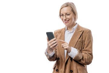 Fototapeta premium Positive woman in formal wear using modern smartphone while standing over white background. Business lady in eyeglasses working on cell phone in studio.