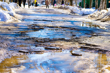 A broken sidewalk. Puddles on the sidewalk due to thawed snow. The concept of poor-quality paving slabs. a sidewalk washed away by water. Close-up.