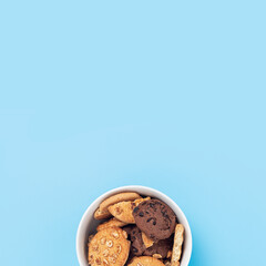 Cookies with chocolate and nuts in a white bowl on a blue background. Top view, flat lay.