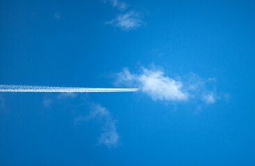 A white stripe from an airplane in a blue sky with white clouds. Flying an airplane high in the sky. Air travel by plane.