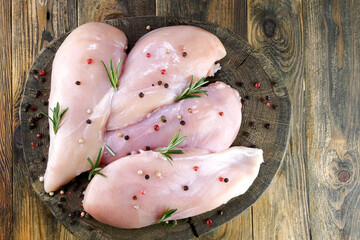 Fresh raw chicken breast fillets sprinkled with peppercorns and rosemary on round wooden board. - 493775265