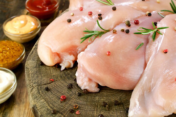 Fresh raw chicken breast fillets sprinkled with peppercorns, rosemary and sauces, on round wooden board. - 493775280