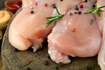 Fresh raw chicken breast fillets sprinkled with peppercorns, rosemary and sauces, on round wooden board. - 493775286