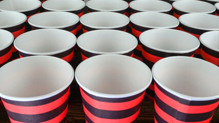 Row of red and black disposable eco friendly paper cup for coffee or hot beverage on dark backdrop. Selective focus. - 493775448