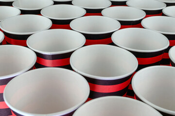 Row of red and black disposable eco friendly paper cup for coffee or hot beverage on dark backdrop. Selective focus. - 493775455