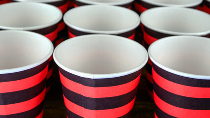 Row of red and black disposable eco friendly paper cup for coffee or hot beverage on dark backdrop. Selective focus. - 493775457