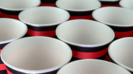 Obraz na płótnie Canvas Row of red and black disposable eco friendly paper cup for coffee or hot beverage on dark backdrop. Selective focus.