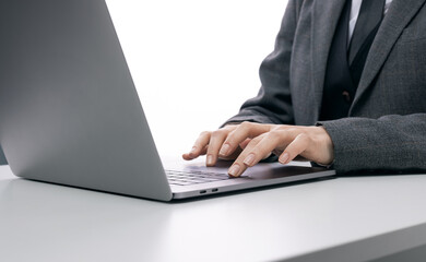 Woman in formal clothes sitting at white table and working on modern laptop. Close up of female hands typing on portable computer.