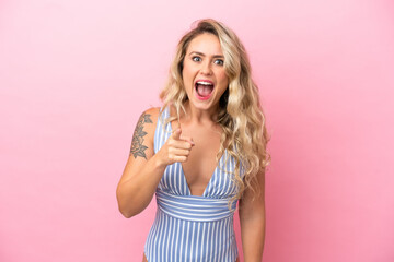 Young Brazilian woman in swimsuit in summer holidays isolated on pink background surprised and pointing front