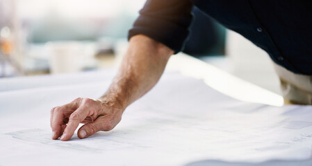 Attention to detail is vital in his line of business. Shot of an unrecognizable architect working on a blueprint in his office.