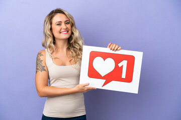 Young Brazilian woman isolated on purple background holding a placard with Like icon with happy expression