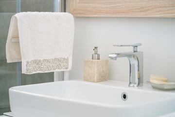 hanged towel and liquid soap bottle by white sink in domestic bathroom