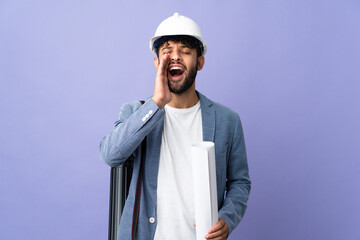 Young architect Moroccan man with helmet and holding blueprints over isolated background shouting with mouth wide open