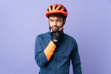 Young Moroccan cyclist man isolated on purple background having doubts and thinking - obrazy, fototapety, plakaty