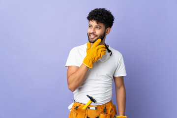 Young electrician Moroccan man isolated on purple background looking up while smiling