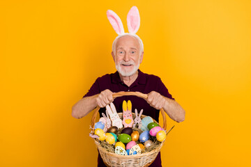 Photo of handsome senior man present party wear bunny ears sweet pastry isolated over yellow color background