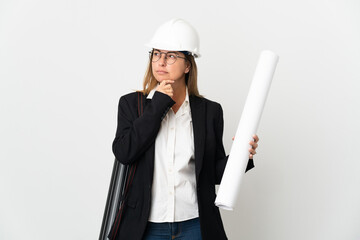Middle age architect woman with helmet and holding blueprints over isolated background and looking...