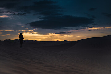Silhouette of a woman standing alone in the dunes of a desert in sunset time.