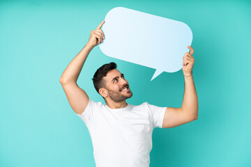 Young handsome caucasian man isolated on blue background holding an empty speech bubble