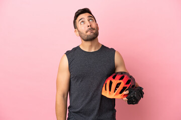 Young cyclist man isolated on pink background and looking up - obrazy, fototapety, plakaty