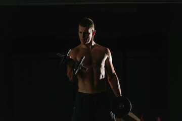 Fototapeta na wymiar Close up dark portrait of a shirtless young man exercising dumbbell alternate biceps curl
