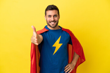 Young handsome caucasian man isolated on yellow background in superhero costume and making a deal