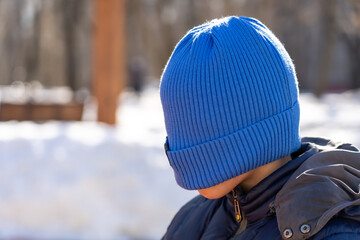 Teen boy pulled blue knitted hat over his eyes to hide his face from the camera lens, family lifestyle