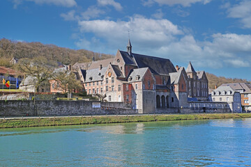 Fototapeta na wymiar Dinant, Belgium - March 9. 2022: View over river meuse on medieval government building cpas aiginst blue sky, fluffy clouds
